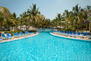 alt="Crystal blue resort style pool surrounded by lawn chairs and palm trees in a South Florida 55+ community."
