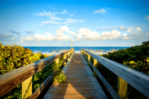 alt="Wooden walkway leading to the beach with blue skies in the background to signify waterfront properties."